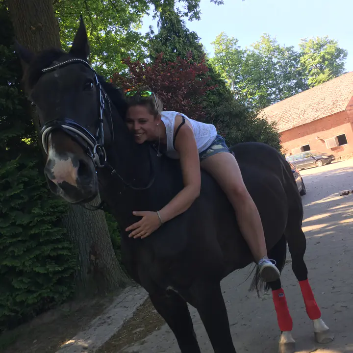 Caro liegt lachend auf dem Hals ihres dunklen Pferdes und umarmt es